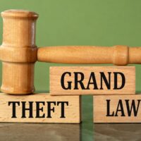 Wooden gavel on blocks saying "GRAND THEFT LAWYER" against a green background.